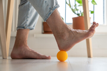 Close up of man rolling small silicone ball under foot while working remotely, improving blood...