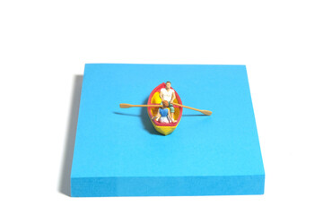 Creative miniature people toy figure photography. Sticky notes installation. A couple dating on a boat at river lake sea. Isolated on white background