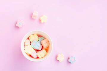 Fototapeta na wymiar Flower Shaped Marshmallows out of a pink paper cup with white dot on pink background, Multicolored Marshmallows