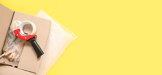 Packing tape dispenser, cardboard box, parcel and bubble wrap on yellow background with space for...