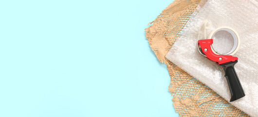 Packing tape dispenser, bubble wrap and paper on light blue background with space for text