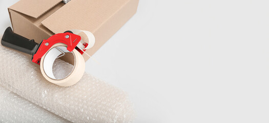 Packing tape dispenser, cardboard box and roll of bubble wrap on light background with space for...