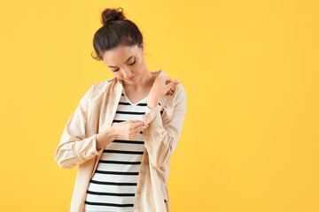 Young woman rolling up her sleeve on yellow background