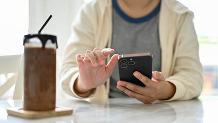 Close-up image of a woman in a comfy sweater using her smartphone at a table