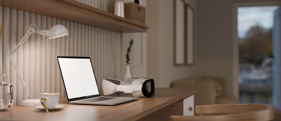 A laptop mockup, modern VR goggles on a wooden table in a minimalist home living room.