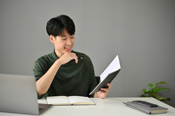 A handsome Asian man checks his meeting schedules in his personal planner book