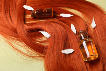 Composition with ginger hair strand, bottles of essential oil and flower petals on green...