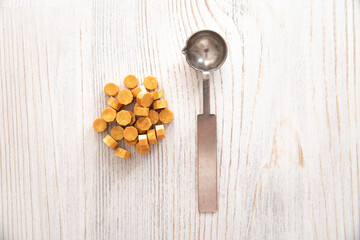 Sealing wax metal spoon, yellow golden sealing wax granules beads on wooden table. Top view