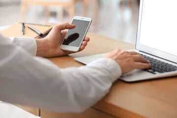 Businessman with smartphone and laptop in office, closeup