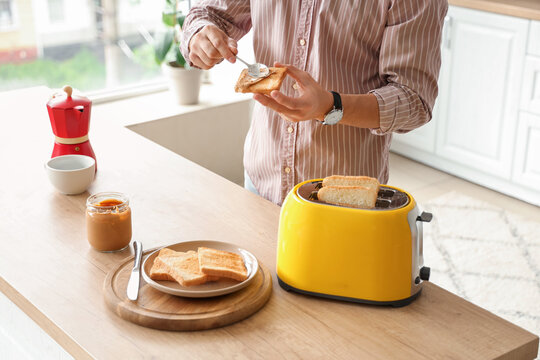 Young man making toast with tasty nut butter in kitchen