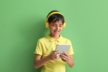 Little boy in headphones using tablet computer on green background