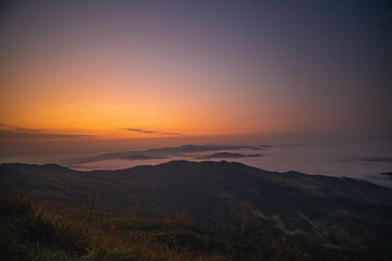The stunning view from a tourist's standpoint as they go down a hill on a foggy trail with a hill and a background of a golden sky in Phu Langka Forest Park in Phayao, Thailand.