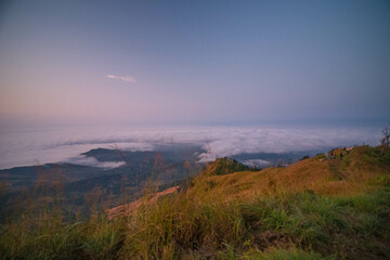 The stunning view from a tourist's standpoint as they go down a hill on a foggy trail with a hill and a background of a golden sky in Phu Langka Forest Park in Phayao, Thailand.