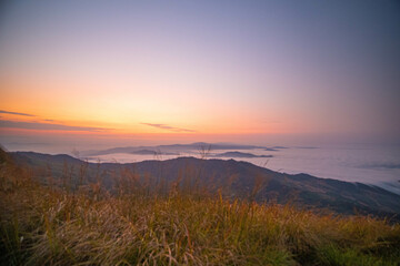 The stunning view from a tourist's standpoint as they go down a hill on a foggy trail with a hill and a background of a golden sky in Phu Langka Forest Park in Phayao, Thailand.