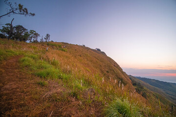 The stunning view from a tourist's standpoint as they go down a hill on a foggy trail with a hill and a background of a golden sky in Phu Langka Forest Park in Phayao, Thailand.