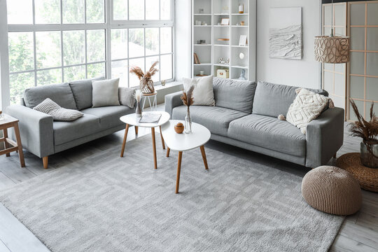 Interior of light living room with cozy grey sofas and coffee table near big window