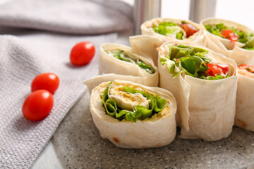 Board of tasty lavash rolls with tomatoes, egg and greens on table