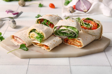 Board of tasty lavash rolls with vegetables on white tile background