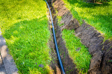 A ditch dug in the lawn for laying pipes and installing irrigation. Soil under green lawn and grass root system