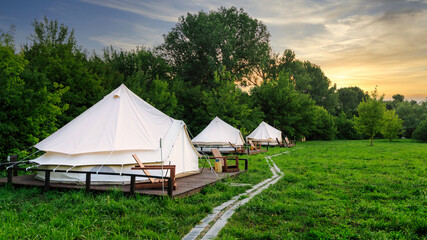 Fototapeta na wymiar Glamping tents in nature with green grass at sunset. Summer season