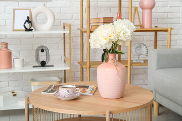 Vase of white peonies on coffee table, couch and shelving unit near white brick wall