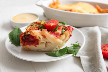 Plate and baking dish of pasta with tomato sauce on white wooden background