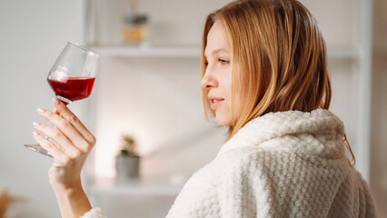 Spa alcohol. Weekend drink. Vacation toast. Blonde woman in bathrobe with glass of red wine on light interior free space background.