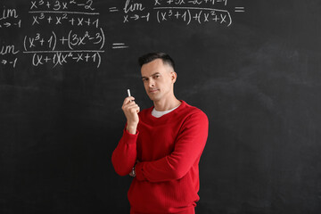 Male Math teacher with chalk piece near blackboard in classroom