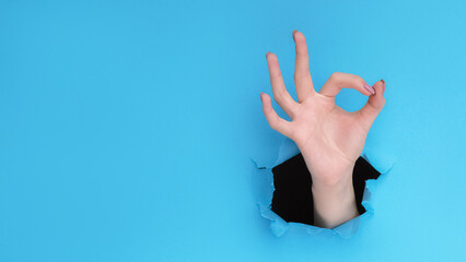 OK gesture. Perfect choice. Female hand showing approval finger circle sign inside ripped wall...