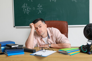 Stressed male teacher sitting at table in classroom