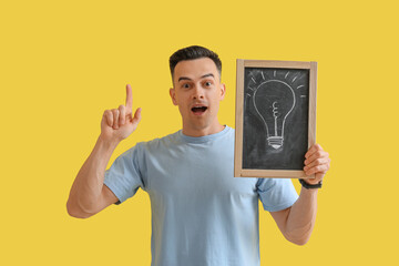 Male teacher holding chalkboard with drawn light bulb on yellow background