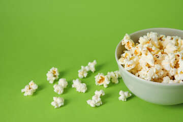 Bowl with tasty popcorn on green background