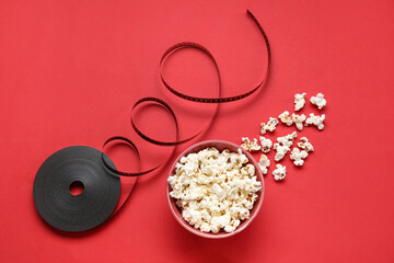 Bowl with tasty popcorn and film reel on red background