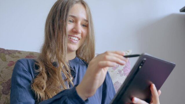 Happy woman working on tablet from the sofa. Young adult using a touch screen tablet, in Slow Motion