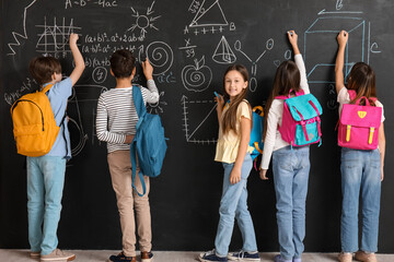 Little pupils with backpacks near blackboard, back view