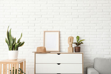 Interior of light living room with drawers, blank frame and houseplants