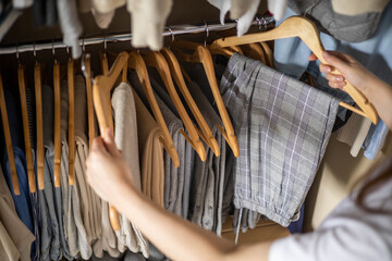 A woman chooses her trousers in the wardrobe. The concept of a harmonious capsule wardrobe.