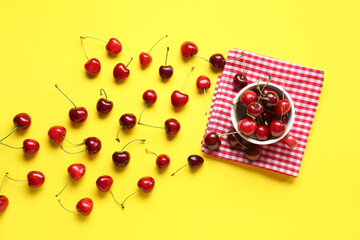 Cup with sweet cherries on yellow background