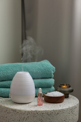 Essential oil aroma diffuser humidifier diffusing water articles in the air. Spa and health care concept. Epsom salt, terry towels, candles, aroma oil.