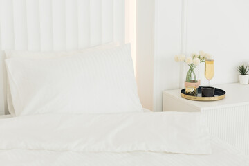 Bedroom interior with white bed. a glass of champagne and flowers on the table.