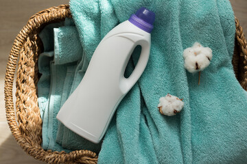 White plastic packaging with laundry detergent, liquid washing powder, conditioner, bleach, stain remover for clothes, terry towels and cotton flowers in a basket.