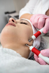 Beautician doing facial procedures with electrical impulses tool at spa salon