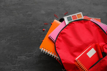 Naklejka premium Red school backpack with notebooks, watercolors and paper clips on black background