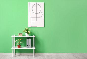 Shelf unit with folders and houseplants near green wall