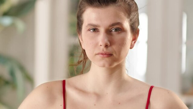 A young brunette look serious at camera. Sport woman doing exercices at home for weight loss. Serious woman think about fat loss, she decide to make exercises at home