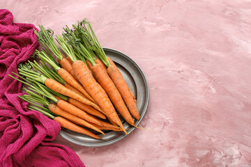 Plate with fresh carrots on pink background