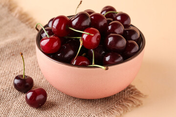 Bowl with sweet cherries on orange background