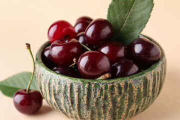 Bowl with sweet cherries and leaves on beige background