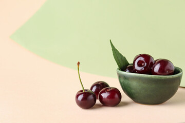 Bowl with sweet cherries and leaf on colorful background