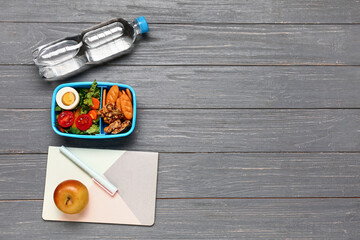 Bottle of water, stationery and lunchbox with tasty food on grey wooden background